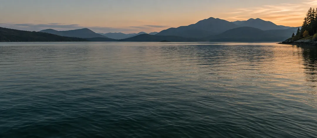 Still mountain lake at dusk under a warm sky.